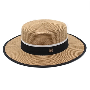 Detail of flat top boater hat with woven straw texture and black ribbon with gold M logo