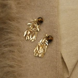 Detail view of golden leaf tassel earrings with brown round beads on brown knit fabric