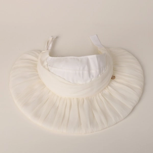 Detail of cream sun hat showing pleated mesh texture and a gold decorative emblem