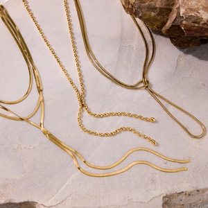 Detailed view of three gold-plated stainless steel chains on a textured stone base