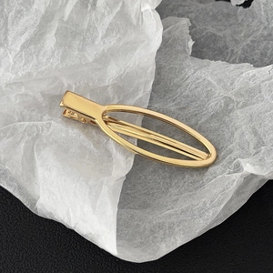 Detail view of a polished golden oval alloy duckbill hair clip on a textured surface