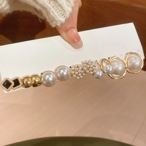Close-up of elegant hair clip with pearls, black geometric square and golden metal rings