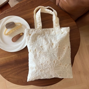 Detail of delicate white lace embroidery on a vintage style cotton tote bag on wood