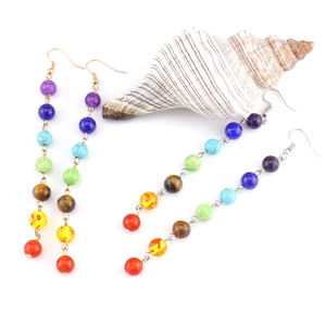Detail of colorful chakra natural stone bead tassel earrings on a decorative seashell
