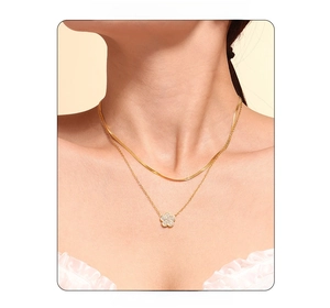 Detail of layered gold clover necklace with snake chain and zircon flower pendant