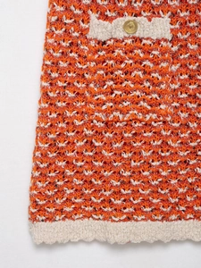 Detail of orange textured knit dress featuring a gold embossed button and contrast trim
