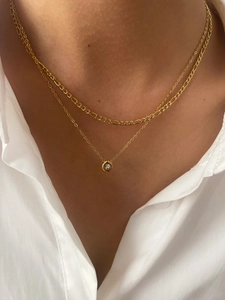 Detail of layered 18K gold Figaro chain necklace with round zircon pendant on white shirt