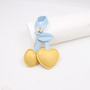 Detail of yellow leather cherry keychain with blue leaf and golden metal clip