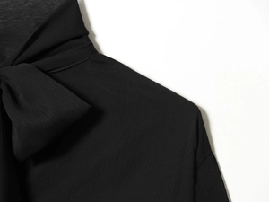 Detalle de una blusa negra de gasa con un elegante cuello de lazada y tejido con textura