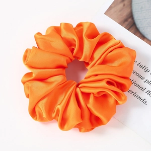 Close-up of a large bright orange satin oversized scrunchie with a glossy silk texture