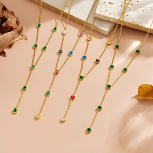Detail of four golden Y-shape necklaces with colorful heart and oval gemstones on marble