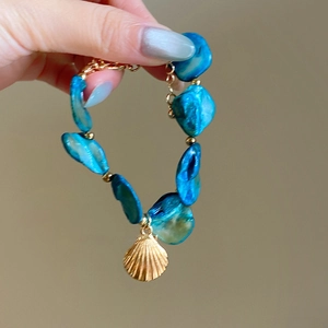 Detail of blue shell bead bracelet with gold shell pendant and small golden spacer beads