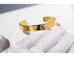Detail of a polished gold-plated open bangle featuring a minimalist smiling face motif