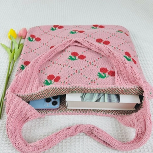 Detailed knit tote bag with cherry pattern, holding a smartphone and a white book