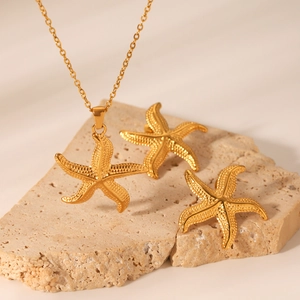 Parure collier et boucles d'oreilles étoile de mer dorée sur fond de pierre beige