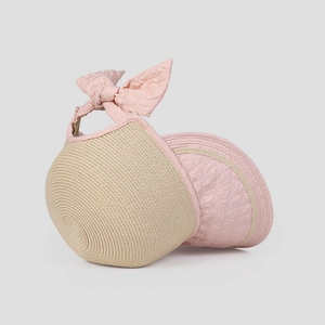 Detail view of beige straw sun hat with textured pink trim and a large elegant bow