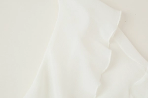 Detailed macro view of white ruffle trim and breathable knit texture on a V-neck blouse