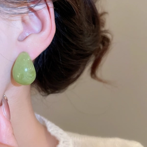 Close-up of green resin teardrop earring with marble texture worn by a model