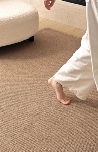 Close-up of bare feet on a light brown faux sisal rug with a woven texture and anti-slip backing