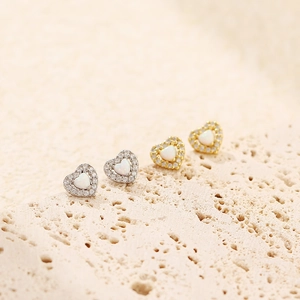 Macro shot of heart-shaped opal stud earrings with diamond halo in gold and silver