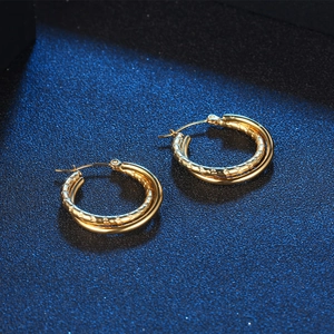 Classic double-layered gold hoop earrings with textured finish on a dark background