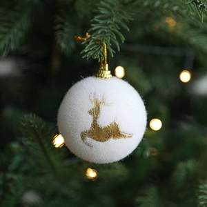 White flocked Christmas ball with gold glitter reindeer hanging on a pine tree