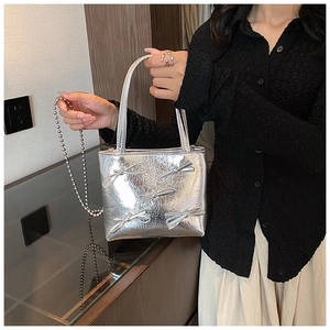 Detail of silver metallic handbag featuring a bow ornament and elegant chain strap