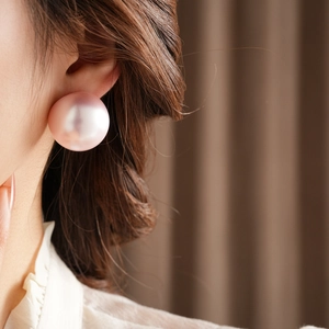 Detailed close-up showing a large pink pearl stud earring worn on a model's ear
