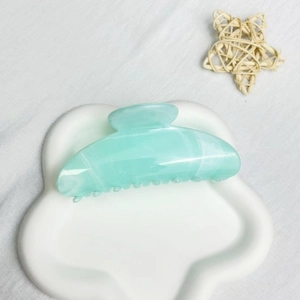 Detail view of large mint green claw clip with marble texture on a white tray