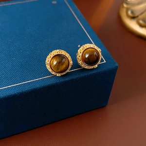 Detailansicht der goldenen Tigerauge-Ohrstecker auf einer blauen Schmuckschatulle
