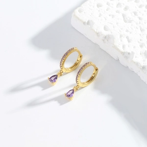 Macro detail of gold S925 silver earrings with purple teardrop zircon on a stone base