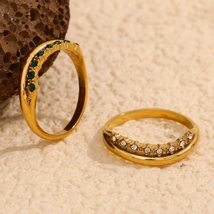 Nahaufnahme von doppellagigem Goldring mit grünem Edelstein und weißem Zirkon auf Stein
