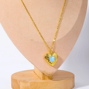 Golden heart locket pendant with blue opal and etched floral pattern on a jewelry bust