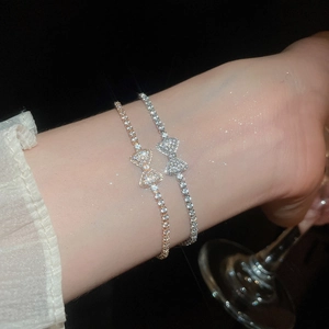 Close-up of sparkling bow pendant tennis bracelets in rose gold and silver on a model's wrist