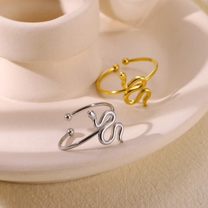 Close-up of snake-shaped open rings in gold and silver finish on ceramic base