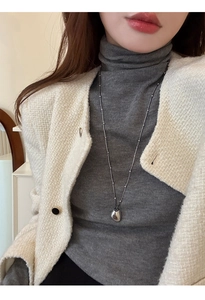Detail of a silver teardrop pendant necklace layered over a cozy grey turtleneck sweater