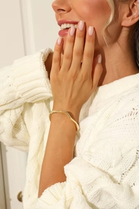 Detail of a wavy 18k gold plated stainless steel cuff bracelet on a model's wrist