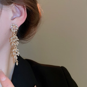 Détail de boucles d'oreilles pampilles dorées avec strass sur un mannequin en blazer noir
