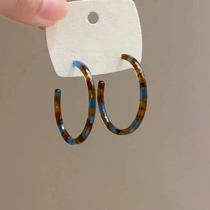 Detailed close-up of C-shaped resin hoop earrings featuring blue and tortoiseshell patterns