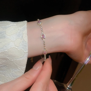 Detail of pink zircon oval bracelet on wrist with gold plating and white lace sleeve