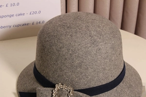 Gros plan sur un chapeau cloche en laine grise avec ruban bleu et boucle en strass