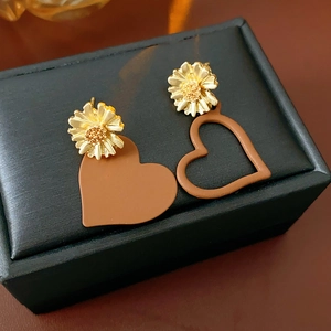 Detail of asymmetric gold daisy earrings with brown heart charms on a jewelry box