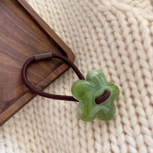 Close-up of green floral hair tie with elastic band on white knit sweater background