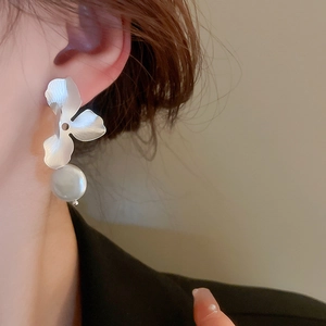 Close-up of silver metal flower earrings with white pearl pendants worn on ear