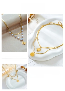Detail of layered gold necklaces featuring butterfly, pearl, and tree of life pendants