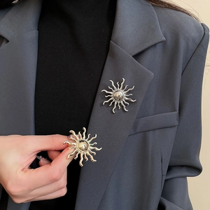 Close-up of gold and silver sun brooches on a grey blazer showing metal textures