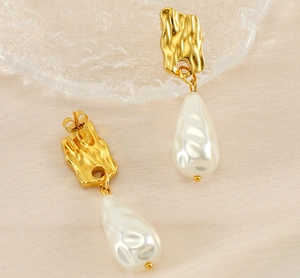 Macro detail of hammered gold rectangle stud earrings with baroque pearl drops on silk