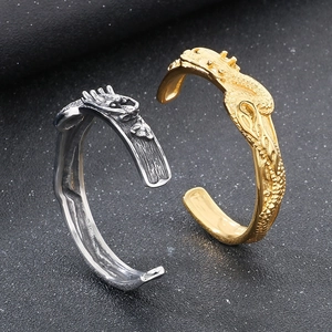 Dettaglio di bracciali a testa di drago in oro e argento con trame a scaglie incise