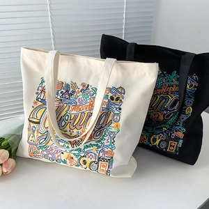 Close-up of colorful embroidery details on cream and black canvas tote bags