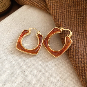 Detailed shot of 18k gold plated amber resin earrings on beige burlap and knit background